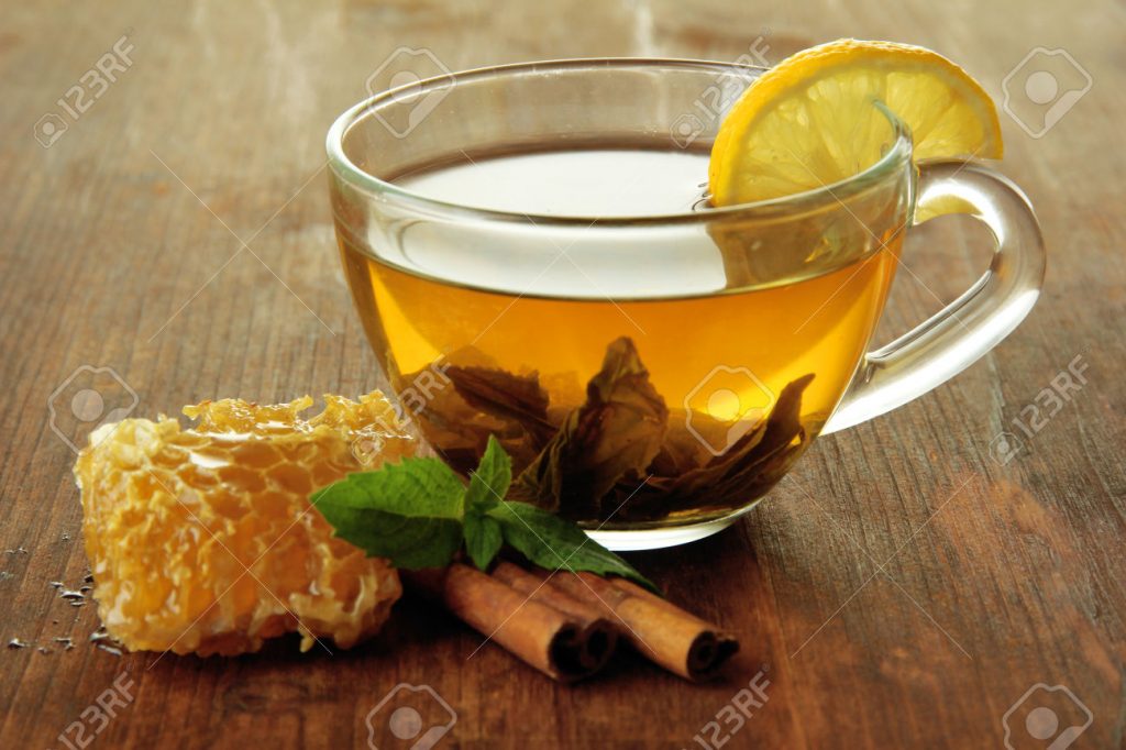 Transparent cup of green tea with honey and cinnamon on wooden background